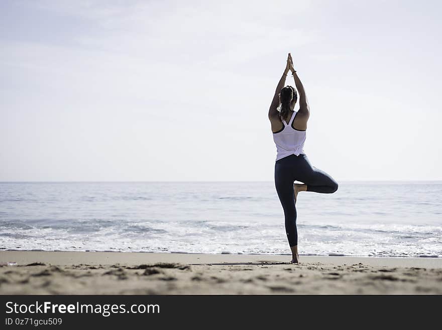 Sporty young woman doing Yoga exercises using a gym mat along the beach in Lisbon, Portugal. Playful woman working as freelance Yoga teacher doing fitness workout on the beach at sunset. Healthy life