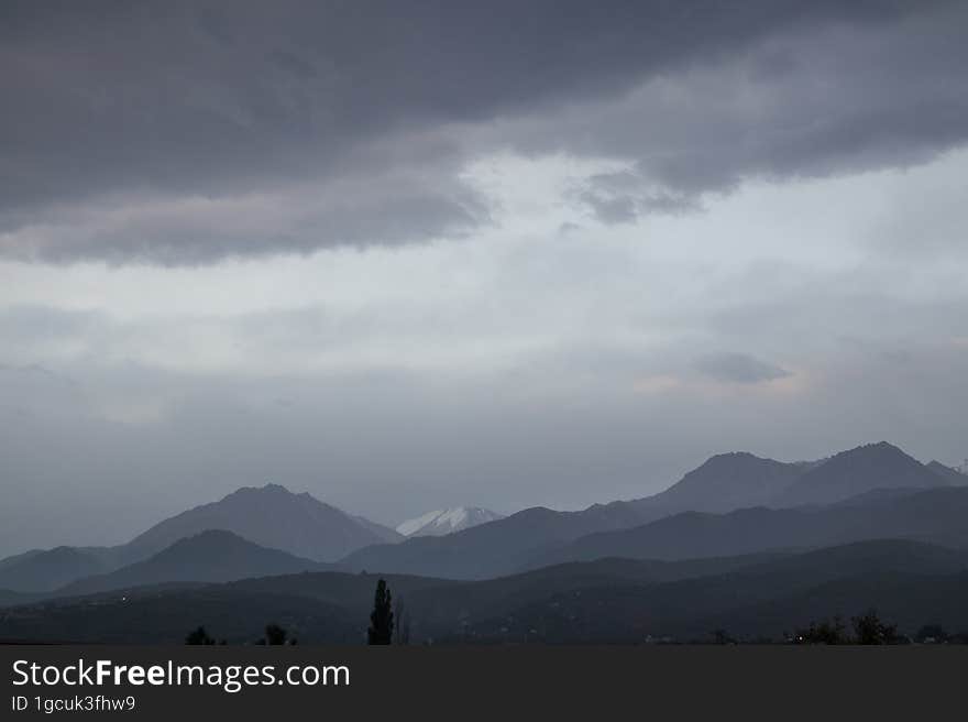 Landscape of the Trans-Ili Alatau mountains on an early cloudy morning in the morning fog with thunderous gray large clouds