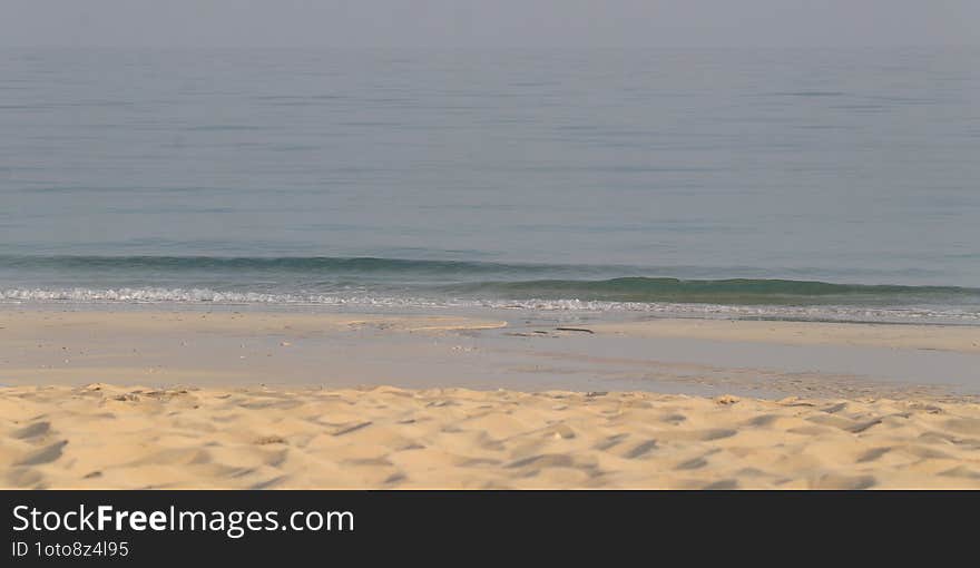 Calm Shoreline. Gentle waves roll onto a quiet sandy beach, creating a peaceful and undisturbed landscape. The calm sea stretches into the horizon, blending seamlessly with the soft sky above.