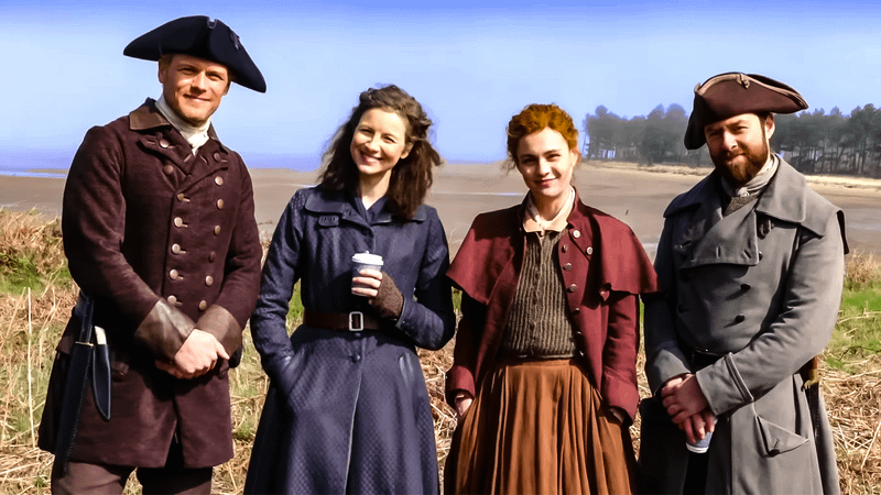 The Outlander cast standing in a field in old-timey wear