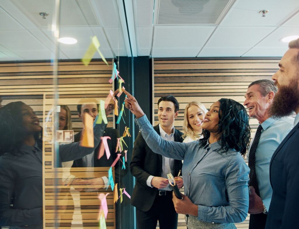 A group of individuals brainstorming ideas by placing sticky notes on a reflective wall surface