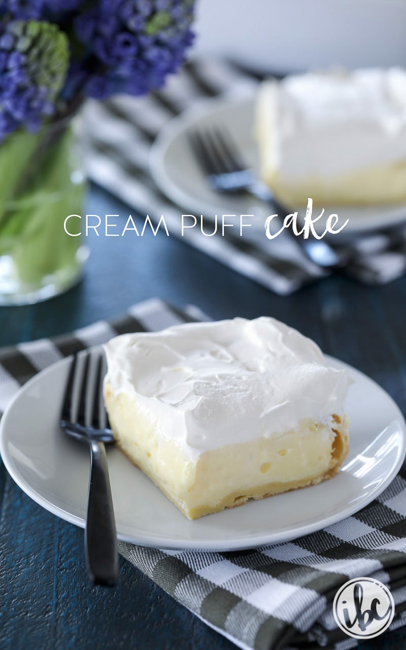 piece of cream puff cake on a plate with a fork on a gingham napkin.