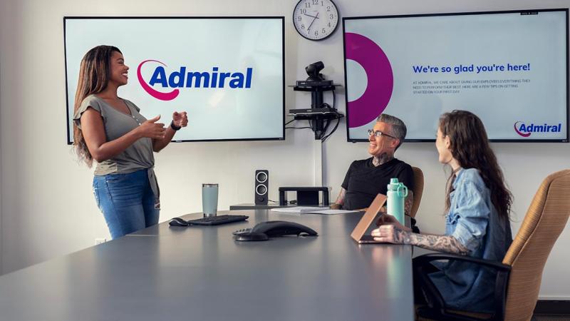 Three people meeting in a conference room. Large screens in the background show the Admiral logo.