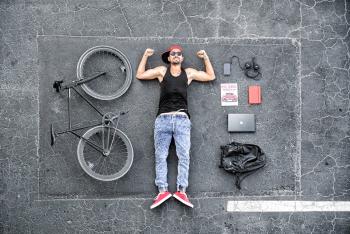 Man in Black Tank Top Laying on Gray Concrete Surface Near Black Bike