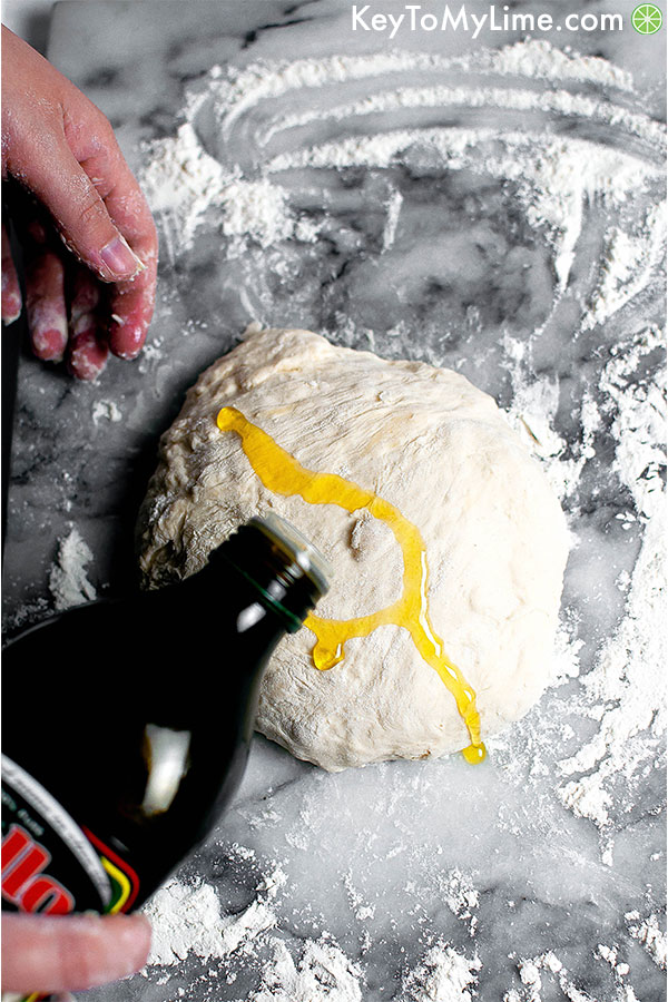 Pouring olive oil on pizza dough ball.