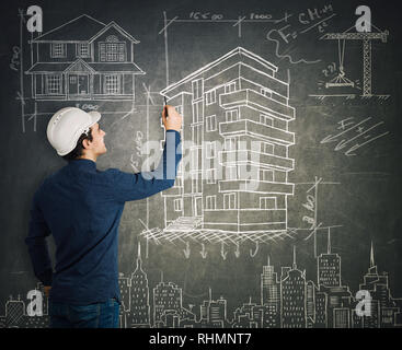 Rear view of creative young man construction engineer or architect wearing protective helmet confident drawing different project sketches on blackboar Stock Photo