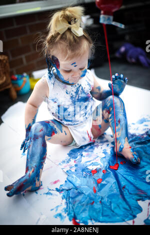 Un adorabile piccolo bambino, ragazza è divertente giocare con la colorazione di pitture, getting confuso e divertirsi un sacco, girato in un ambiente domestico Foto Stock