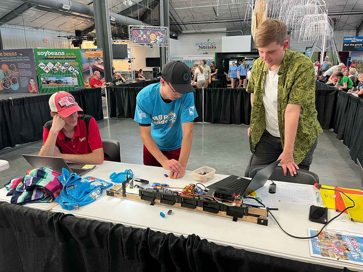 three young men looking at a robot with legos nearby