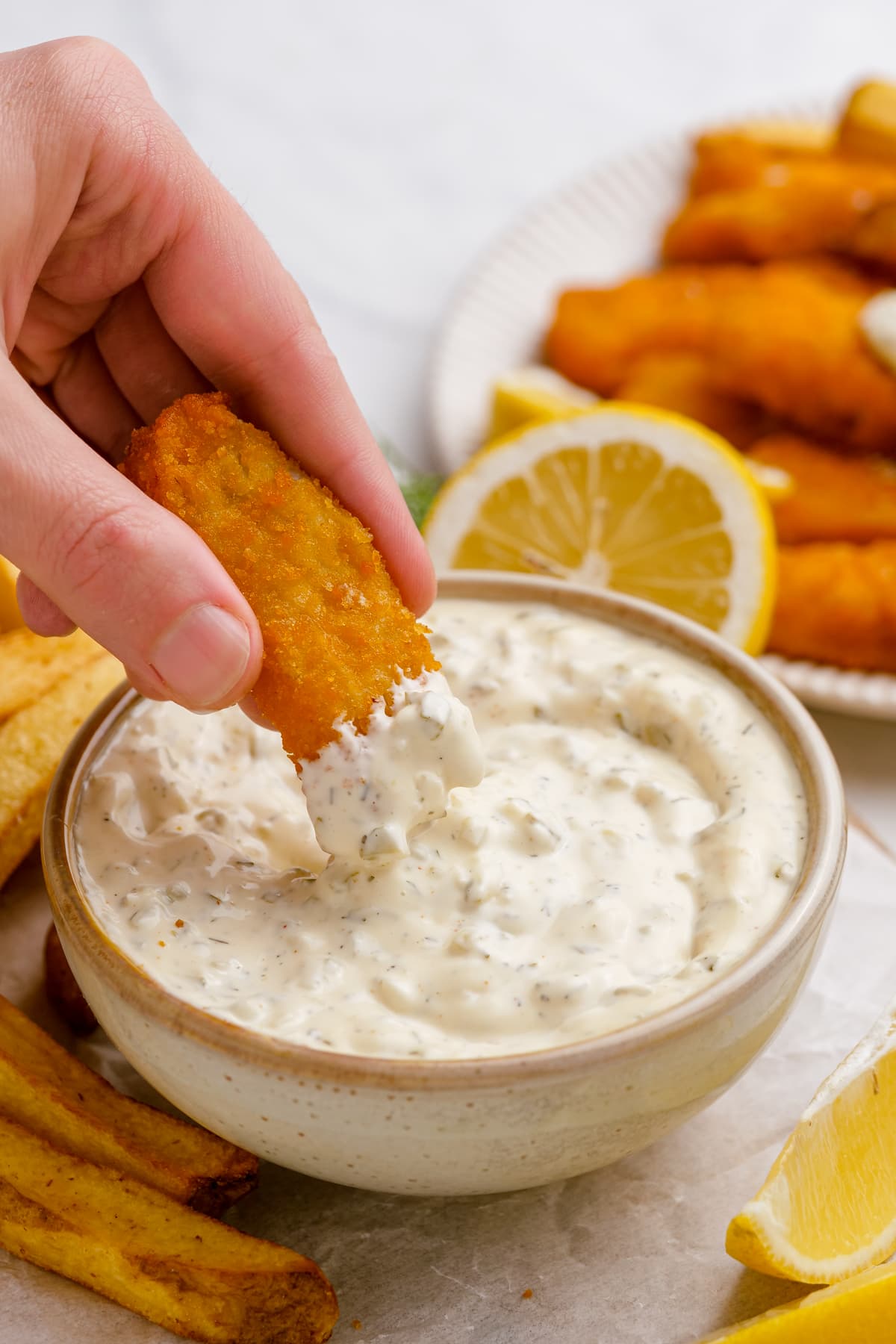 woman's hand dipping fish stick into bowl of tartar sauce