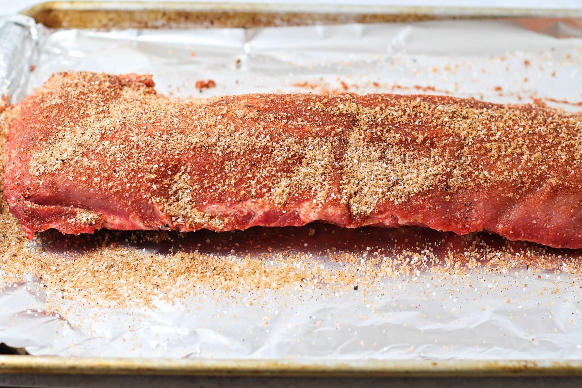 Seasoning ribs with a dry rub on a lined baking sheet.