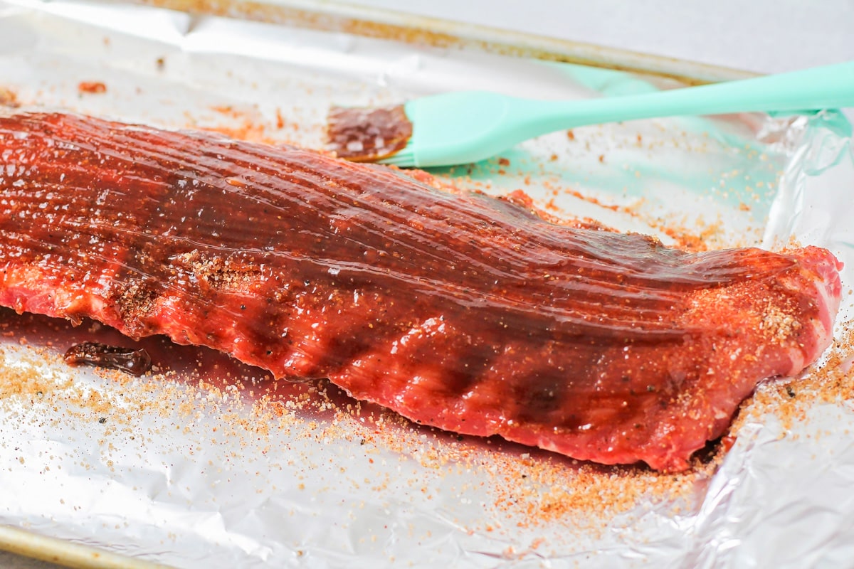 Slathering bbq sauce on baby back ribs before cooking.