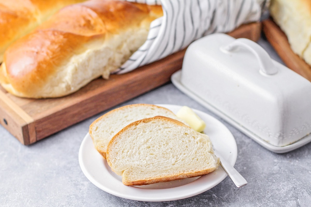 Freshly baked and sliced french bread recipe served with butter on a white plate.