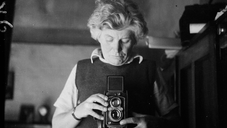 A black and white self portrait - a short haired woman wearing a vest stares into an old Box Brownie camera