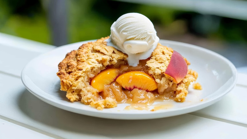 A plate of peach cobbler, its pastry top is golden and pieces of canned peaches are visible in the open slice.