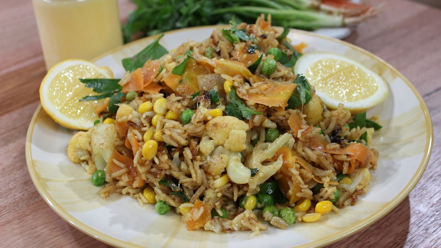 A rice and cauliflower dish on a plate with fresh herbs and lemon cheeks on top and the side