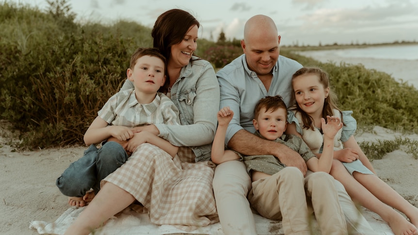 Family with parents, three kids sitting on sand dunes at beach