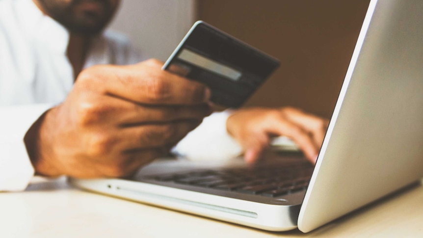 A close up of a man's hand holding an obscured credit card while the other hand types on a laptop.