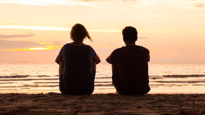 The silhouette of two young people looking out onto a beach at sunset