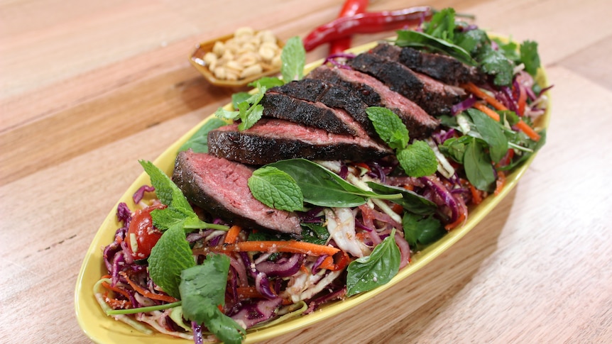 A salad with sliced beef on a bed of veggies with herbs on top