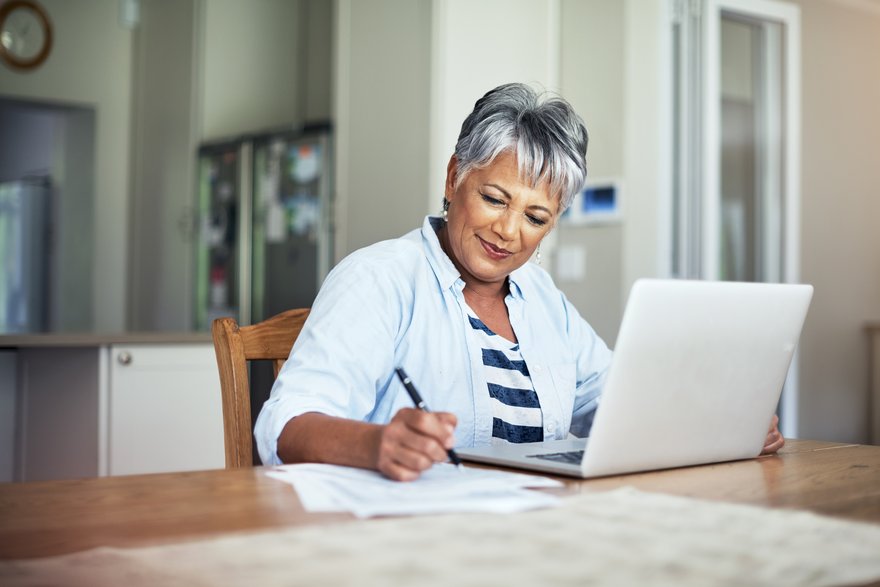 Smiling person takes notes in front of laptop at home.