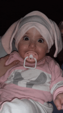 a baby with a pacifier in her mouth is wearing a pink and white outfit