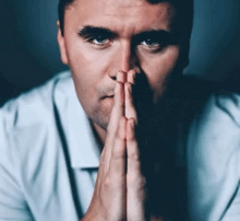 a man in a white shirt is praying with his hands folded in front of his face