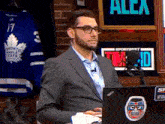 a man in a suit is sitting in front of a laptop with a toronto maple leafs jersey in the background