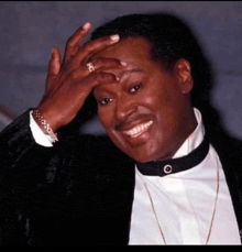 a man in a tuxedo is smiling and covering his face