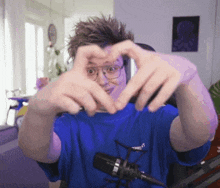 a man wearing glasses and a blue shirt making a heart shape with his hands