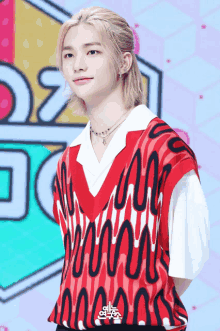 a young man wearing a red vest and a white shirt stands in front of a sign that says ' a ' on it