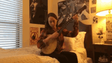 a girl sits on a bed playing a banjo in front of a wall with a beatles poster on it