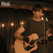 a man singing into a microphone while holding a guitar in front of a how to fail as a popstar sign