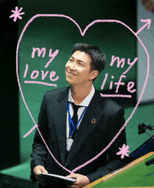 a man in a suit stands in front of a pink heart that says my love my life