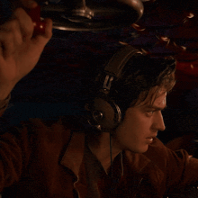 a man wearing headphones and a brown jacket looks at the camera