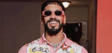 a man with a beard is wearing sunglasses and a pink shirt and smiling .