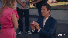 a man in a suit is proposing to a woman in a pink dress with a netflix logo behind him