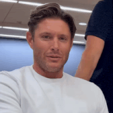 a man wearing a white t-shirt is smiling for the camera