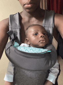 a woman is carrying a baby in a gray carrier