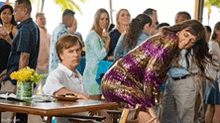 a woman in a purple dress is sitting at a table in front of a crowd .