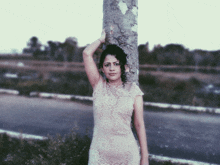 a woman in a white lace dress leans against a tree trunk