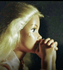 a doll with blonde hair and blue eyes is praying with her hands folded