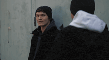 two men standing next to each other one wearing a black beanie and the other wearing a white hoodie