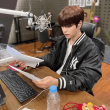 a young man in a ny yankees jacket is sitting at a desk with a microphone and a keyboard .