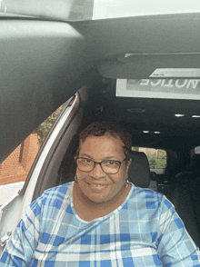 a woman in a blue plaid shirt is sitting in the back seat of a car