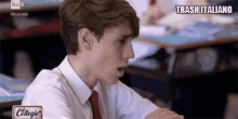 a boy in a white shirt and red tie is sitting at a desk in a classroom with the words trash italiano above him .