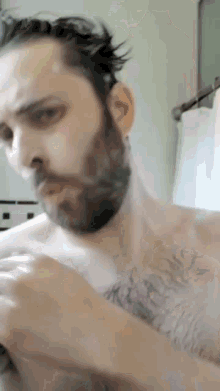 a shirtless man with a beard is shaving his face with a razor