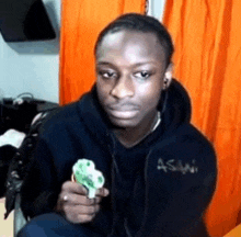 a young man in a black hoodie is holding a green object in his hand .