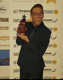 a man holding a trophy in front of a wall that says compass today