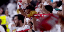 a young boy is holding a red and white scarf in a crowd of people at a soccer game .