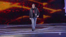 a man in a leather jacket is walking on a stage in front of a wwe logo